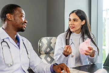 Two cardiologists engage in a detailed discussion on heart disease treatment, using an anatomical model to illustrate their points while consulting with a medical intern in a clinic, share knowledge