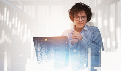 Young businessman with glasses working on laptop, overlaid with abstract financial graph lines and cityscape, on bright office background, concept of business strategy