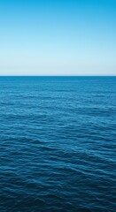 Obraz premium Expansive blue ocean surface stretching towards a distant horizon under a clear sky, showcasing calm yet powerful natural liquid movement ,serene ,vast ,tranquil