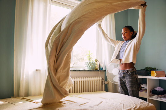 Girl spreading sheet on bed in bedroom at home
