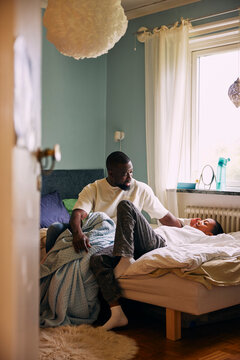 Father spending leisure time talking with son lying on bed in bedroom at home