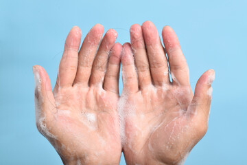 Close-up of hands covered in shampoo foam holding fallen hair strands on blue background, illustrating hair loss and hygiene concept.