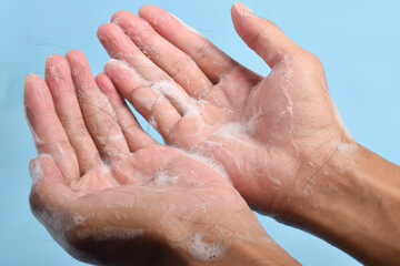 Close-up of hands covered in shampoo foam holding fallen hair strands on blue background, illustrating hair loss and hygiene concept.