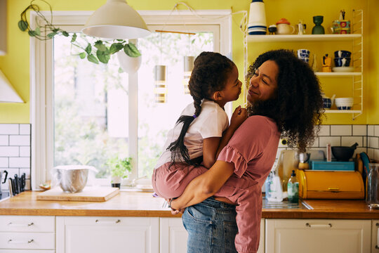 Smiling woman carrying daughter in arms at home