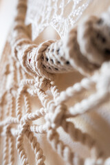Close-up of a handmade macrame wall hanging. The intricate knots and patterns are visible, showcasing the craftsmanship and texture of the natural fibers.