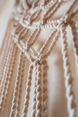 Close-up of a handmade macrame wall hanging. The intricate knots and patterns are visible, showcasing the craftsmanship and texture of the natural fibers.