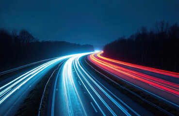 Obraz premium Long exposure shows traffic light trails on a highway at dusk. Cars speed along the dark road surrounded by silhouetted trees. Blue and red lights create abstract patterns.
