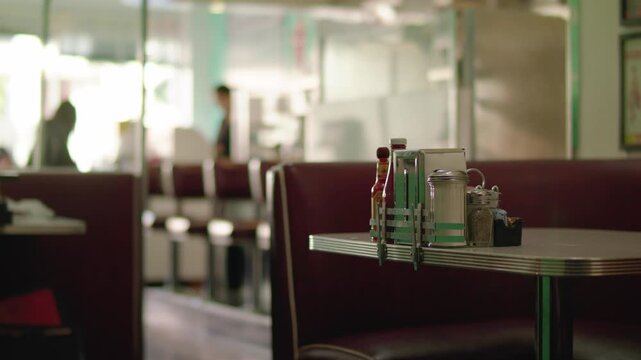 Cinematic View of Empty Diner Booth With Condiments as Waitress and Customer Stand in Background
