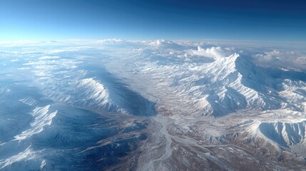 Aerial View of Snow Capped Mountain Range Under a Clear Blue Sky With Sunlight Illuminating Peaks and Valleys