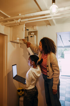 Girl checking wi-fi connection in laptop with mother near electrical outlet at basement