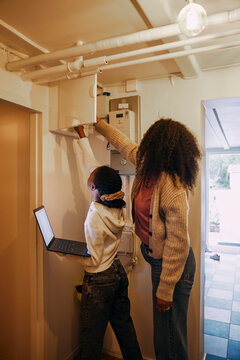 Mother and daughter examining electrical meter for wi-fi connection in illuminated home basement