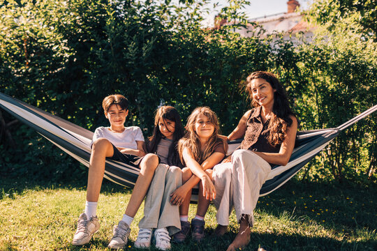 Portrait of smiling mother sitting on hammock with children in garden