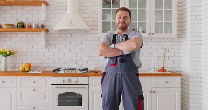 Portrait of confident male plumber standing in kitchen with arms crossed after completing repair work. Smiling professional handyman wearing uniform, ready for maintenance or home improvement tasks.