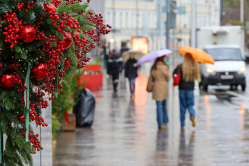 New Year decorations in city, red Christmas balls on a street on blurred background of people with umbrellas during rain