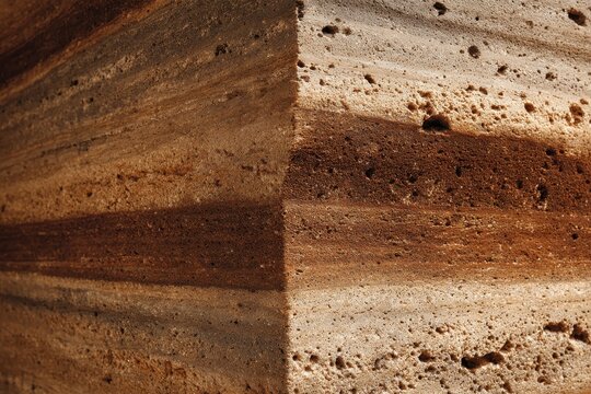 Close-up photo reveals a rammed earth wall's layered texture and earthy tones. Ideal background, illustrating construction, geology, or natural textures.