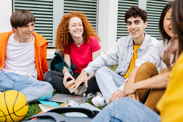 Young group of multiracial teen students sitting on the grass at high school. Millennial generation...
