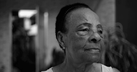 One Elderly Afro-descendant woman in thoughtful profile, looking away from the camera, contemplative expression in an outdoor home setting, natural and intimate