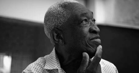 One Elderly Afro-descendant man in black and white portrait, looking upwards with a thoughtful smile, hand touching chin, facial features highlighted in a serene outdoor home setting