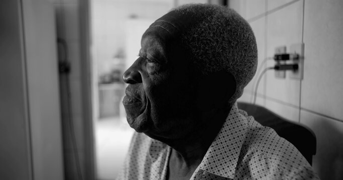 One Elderly Afro-descendant man in black and white profile view, gazing upward with a thoughtful and calm expression, seated in a quiet indoor home setting - Powered by Adobe
