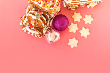 Close-up of a handmade gingerbread train decorated with colorful candies and white icing, surrounded by star-shaped cookies and Christmas baubles on a pink background, top view