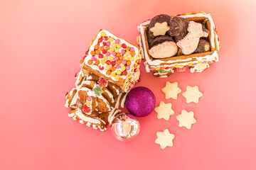  Close-up of a handmade gingerbread train decorated with colorful candies and white icing, surrounded by star-shaped cookies and Christmas baubles on a pink background, top view