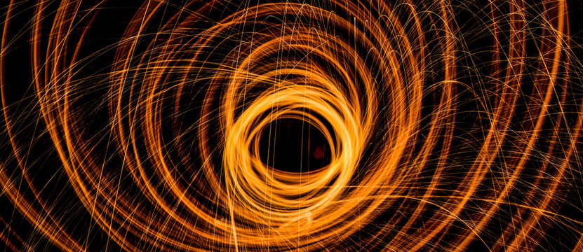 Abstract orange light swirls forming concentric circles in a hypnotic pattern, captured with long exposure photography on a black background, representing energy, creativity, and modern art.

