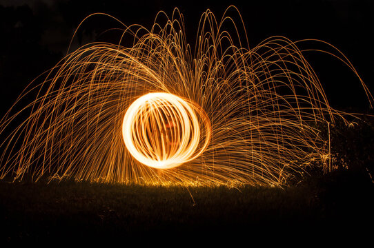 A mesmerizing display of steel wool spinning, creating glowing orange circles and radiant sparks against a dark night background, symbolizing energy, creativity, and dynamic long exposure photography. - Powered by Adobe