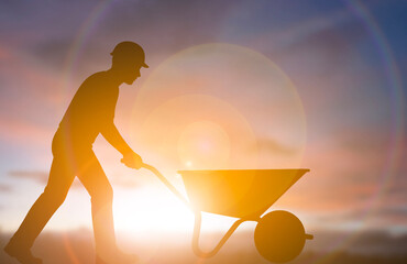 Construction worker pushing wheelbarrow at sunrise silhouette