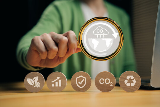 Businesswoman analyzing CO2 reduction and sustainability icons with magnifying glass. Concept of carbon footprint tracking, ESG management, net zero goals, and environmental responsibility.