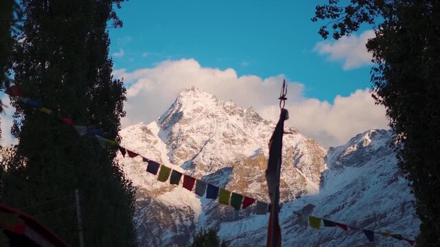 Slow motion shot of defocused prayer flags waving in front of snowy Himalayan mountain peak during the sunset as seen from Keylong in Lahaul and Spiti district, Himachal Pradesh, India. Scenic view. 