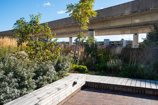 Elevated metro bridge in Stockholm surrounded by green urban park and concrete structure, modern architecture integrated with nature under bright daylight atmosphere