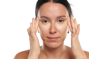 Studio shot of natural woman with dark hair and no makeup applying concealer under eyes with...