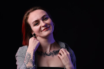 Obraz premium Young woman with piercings, tattoos and stylish clothes on black background, space for text