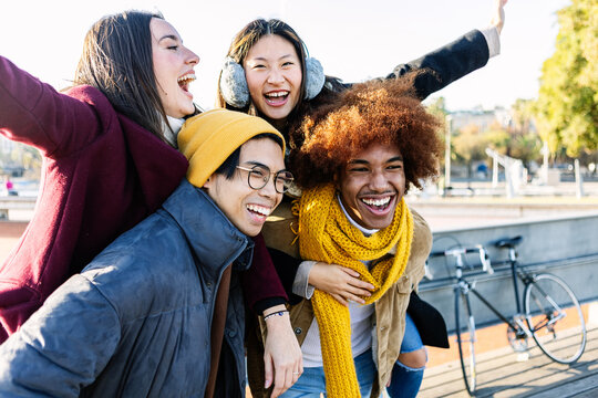 Happy diverse group of friends having fun together on winter season. Millennial people piggybacking outdoors. Youth and friendship concept - Powered by Adobe
