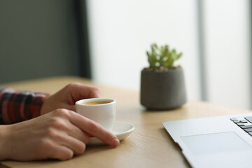 Woman having coffee break at wooden desk indoors, closeup