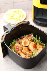 Air fryer basket with grilled chicken drumsticks, spices, green peas and french fries on grey table, closeup