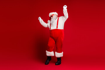 Santa Claus in red suit with suspenders dancing in a bold red studio for festive season and holiday...