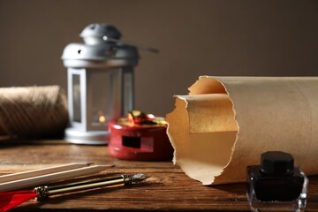 Old paper scroll, fountain pen, pencils and inkwell on wooden table, closeup