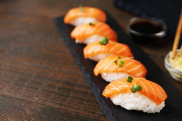 Delicious nigiri sushi with salmon and microgreens on wooden table, closeup. Space for text