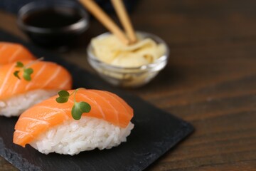 Delicious nigiri sushi with salmon and microgreens on wooden table, closeup. Space for text