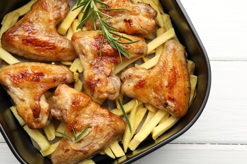 Grilled chicken wings with french fries and rosemary in air fryer basket on white wooden table, top view