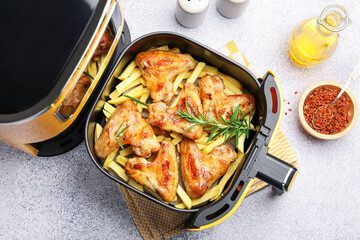 Grilled chicken wings with french fries in air fryer basket and spices on grey table, flat lay