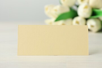 Blank card and flowers on white wooden table, selective focus. Mockup for design