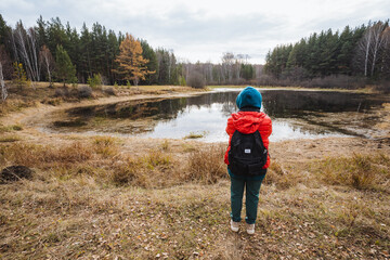 Child gazes afar, Young explorer near water, Child observing distant landscape with curiosity, Young child positioned at lakeside amidst expansive forests prompting adventure and discovery