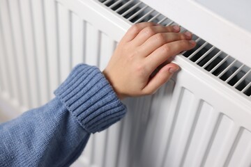 Woman warming her hand near radiator indoors, closeup