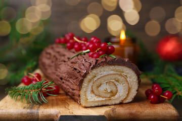Delicious Yule log (traditional Christmas cake) with redcurrant and fir tree branches on table, closeup