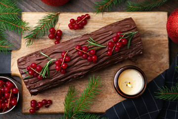 Delicious Yule log (traditional Christmas cake) with redcurrant, decor and fir tree branches on wooden table, flat lay