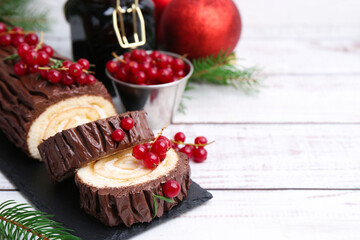 Delicious Yule log (traditional Christmas cake) with redcurrant, decor and fir tree branches on light wooden table, closeup. Space for text