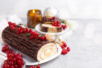 Delicious Yule log (traditional Christmas cake) with redcurrant on gray textured table, closeup. Space for text