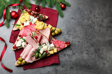 Delicious Christmas Charcuterie board with snacks, fir branches and baubles on grey textured table, flat lay. Space for text
